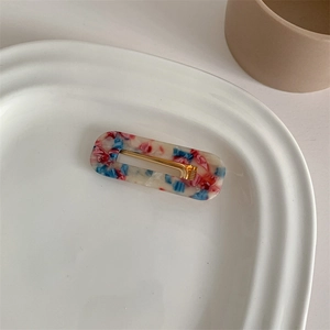 Detailed view of rectangular hair clip with red blue white marble pattern on a ceramic tray