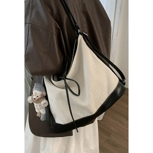 Detail of cream canvas bucket bag with black leather trim and plush bear charm