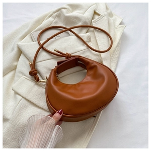 Detailed close-up of a brown leather crescent moon bag on a white tweed jacket surface