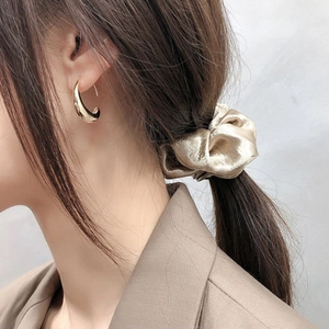 Elegant gold curved C-shape hoop earrings and champagne velvet scrunchie on a female model