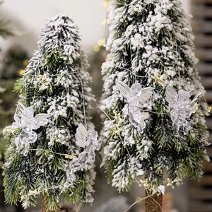 Detailed view of clear acrylic angel ornaments with wings on a snowy Christmas tree branch