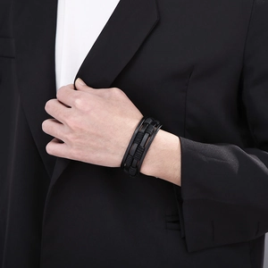 Close-up of men's triple-layer black braided leather bracelet worn with a formal suit