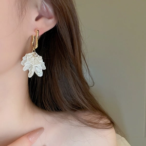 Detail of elegant white acrylic pleated flower earrings with gold plated hoops on model