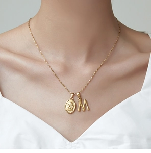 Close-up of a 18K gold plated necklace with an angel relief pendant and letter M charm