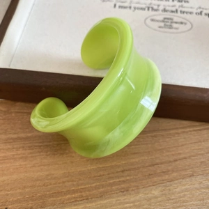 Close-up of lime green resin bangle with irregular organic wave pattern on wooden table