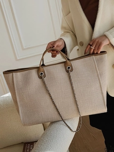 Large beige canvas bucket bag with brown leather handles and decorative metal chains
