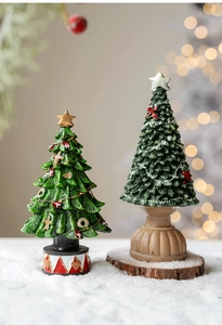 Detailed view of two miniature resin Christmas trees with red and snowy bases on wood