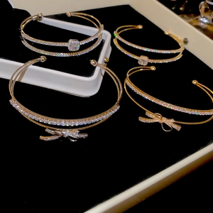 Macro detail of double-layered gold bow bracelets with cubic zirconia on black velvet tray