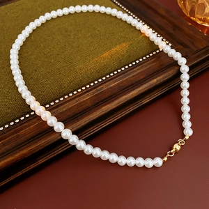 Detail view of round white pearls with a golden magnetic clasp on vintage fabric