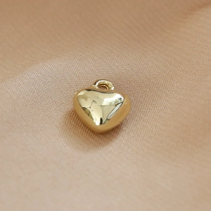 Macro shot of a smooth gold heart pendant with a ring connector on beige fabric