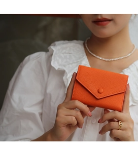 Detail of an orange pebbled leather envelope wallet held by a model in a white shirt