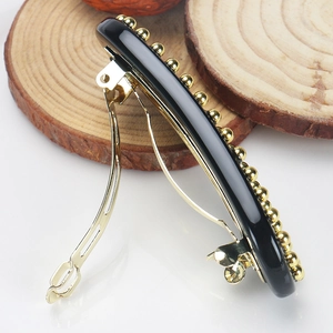 Detailed close-up of a vintage black acetate hair clip with elegant gold pearl accents