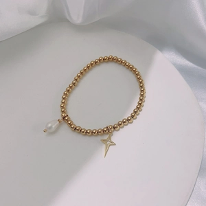 Detail shot of a gold pearl bracelet with a hollow star pendant on a white tray