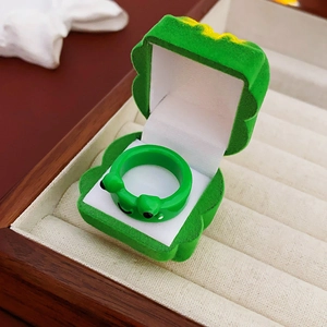 Macro shot of green cartoon frog ring and matching velvet jewelry gift box in wooden tray