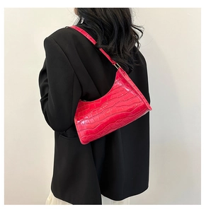 Detail of rose red baguette bag with crocodile texture worn on shoulder over black blazer