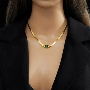 Detail of a gold snake bone chain with an oval green zircon stone on a black suit