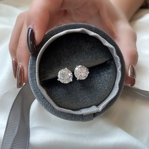 Close-up of classic round-cut zircon studs in a grey velvet gift box on white silk