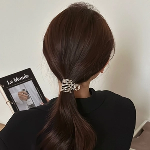 Detail of a silver hollow metal hair claw clip securing a low ponytail on a model