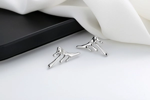 Macro detail of silver liquid lava stud earrings on white silk and dark tray background