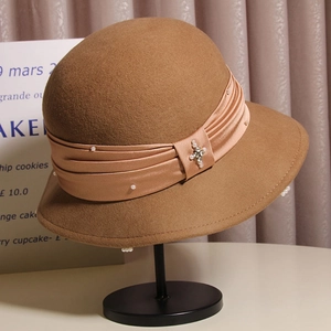 Close-up of brown wool cloche hat featuring satin ribbon, pearls, and a cross jewel