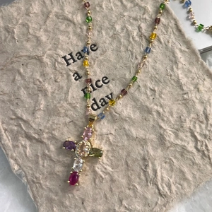 Détail macro d'un collier croix doré avec zircons multicolores et perles colorées