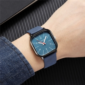 Detail of square quartz watch with blue textured dial and leather strap worn on wrist