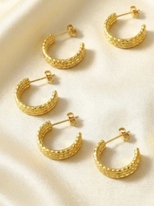 Detail of 18K gold-plated C-shape earrings showing hammered texture on silk background
