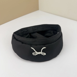 Close-up of black fabric headband featuring an elegant white pearl bow on a beige background
