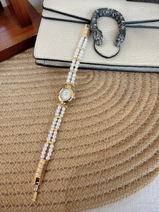 Detail of vintage gold pearl watch on woven mat with textured cream bag background