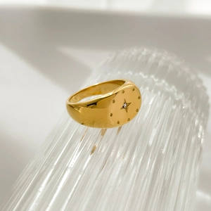 Macro shot of gold signet ring with engraved starburst and inset zircon on textured glass