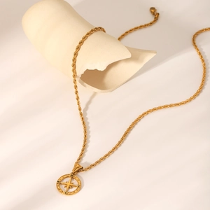 Collana con ciondolo a bussola dorata su supporto in ceramica beige con ombre morbide
