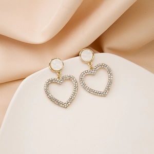Detailed view of heart-shaped gold earrings with white crystals on soft silk background