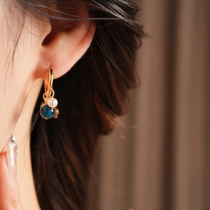 Detail of vintage gold hoop earring with pearl and tiger eye bead tassels worn on ear