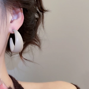 Detailed view of beige acrylic C-shaped earring on model with matte finish