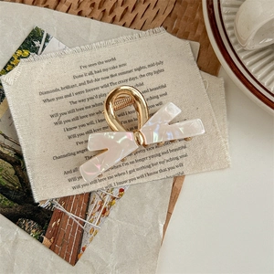 Detail of a white pearlescent acetate bow hair claw with elegant golden metal clip
