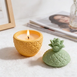 Handmade pineapple scented candle with yellow textured jar and green leaf lid on white rug