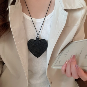 Detail of a black leather heart-shaped eyewear case worn as a stylish sweater necklace