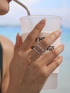 Detail of silver rings with zircons and pearls on a model holding a matte cup