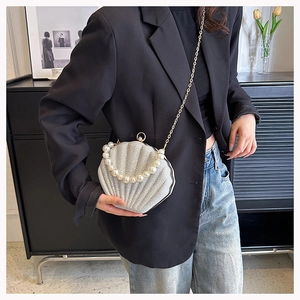 Silver shell-shaped clutch bag with pearl handle and chain worn over a black blazer