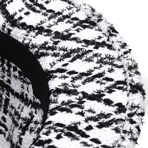Detailed close-up of houndstooth tweed texture with black feather-like fibers and ribbon