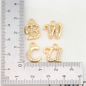 Detail shot of golden rhinestone letter charms B, W, C, U with a ruler for size reference