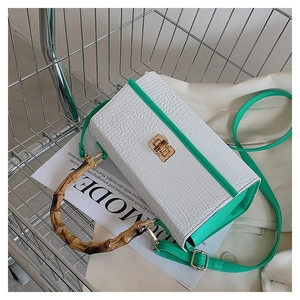 Close-up of white crocodile pattern bag with bamboo handle and green strap in a cart