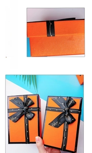 Close-up of elegant orange gift box with black ribbon and golden happy lettering