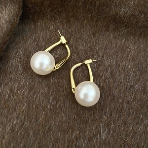 Detailed close-up of large round pearl earrings with gold hooks on dark velvet