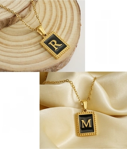 Macro view of 18K gold plated stainless steel square pendant with black enamel letter detail