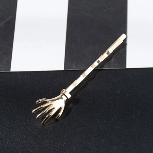 Minimalist golden skeleton hand hair clip with polished metallic finish on striped background