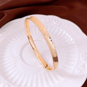 Macro shot of gold-plated fish scale textured bangle on elegant white ceramic and velvet