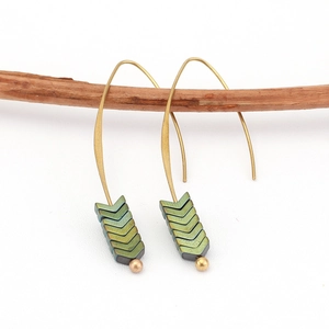 Detail of bohemian arrow earrings with iridescent green V-shapes hanging on a branch