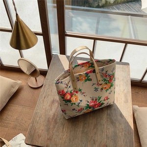 Floral cotton tote bag with leather handles on wooden table in warm light setting
