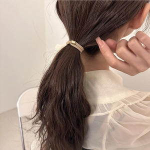 Minimalist elastic hair tie with golden metallic texture worn on a ponytail
